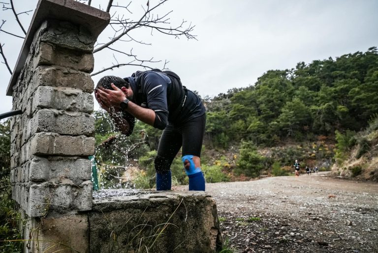A runner at a stone fountain washing face during trail run in Turkish countryside.