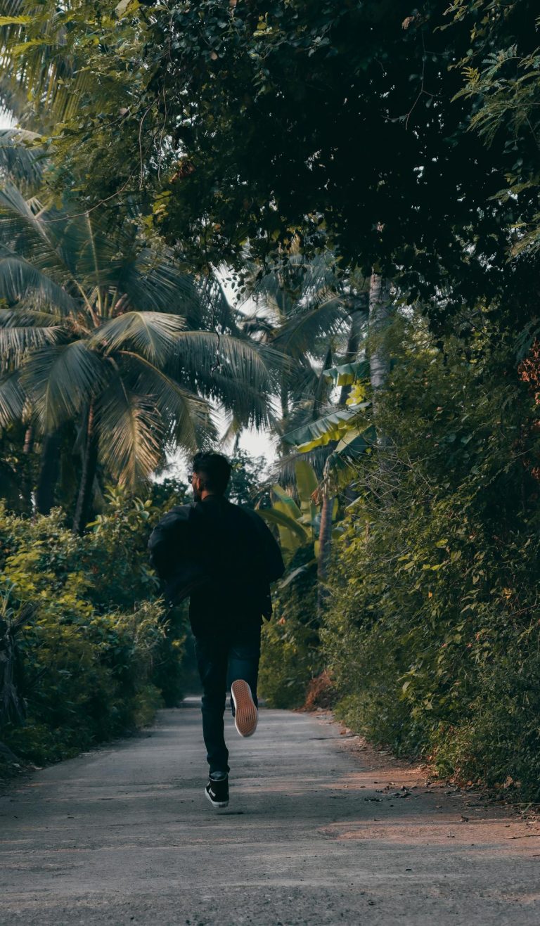 Back view of a man running on a tropical path surrounded by dense foliage.