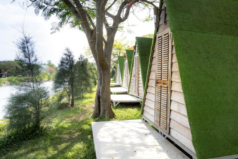 Picturesque scenery of green shore of river and wooden houses with triangular green roof located in row on sunny summer day